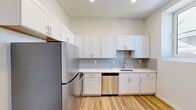 This two-story space is thoughtfully designed with a clean, modern aesthetic and distributes its square footage across two distinct levels. The lower floor houses a well-appointed kitchen featuring white shaker-style cabinetry extending to the ceiling, light gray subway tile backsplash, white quartz countertops, and a full suite of stainless steel appliances including a refrigerator, range, microwave, and dishwasher. A tall window draws natural light into the kitchen area, offering views of the surrounding neighborhood. A striking black metal spiral staircase anchors the lower level, serving as both a functional and architectural focal point, with a hallway leading to a bathroom equipped with large-format tile flooring, a vessel sink vanity, and a bathtub.

The upper floor is characterized by dramatic vaulted, sloped ceilings that lend an open, airy quality to the space. Light hardwood flooring runs throughout, complemented by crisp white walls. Rooms on this level feature wall-mounted mini-split HVAC units for individual climate control, ceiling fans, and skylights that invite abundant natural light. The upper level also includes additional rooms with closet access, providing flexible living arrangements throughout.