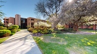 This meticulously maintained outdoor courtyard offers a serene and inviting environment defined by its rich landscaping and classic architectural backdrop. The surrounding multi-story brick building features arched windows, private balconies, and a warm, timeless aesthetic that frames the green space with a sense of permanence and character.

The grounds are thoughtfully designed with a network of smooth concrete walkways that wind through a diverse and layered landscape. Mature flowering trees — including white-blooming crabapples and magnolias — serve as striking focal points, particularly in spring when their blossoms create a canopy of color. Beneath them, dense ornamental shrubs, ground cover plantings, and mulched garden beds provide year-round texture and visual interest.

Well-kept open lawn areas offer a sense of openness and breathing room throughout the courtyard. Classic black lamp posts are positioned along the pathways, adding a traditional, pedestrian-friendly character to the space. Seating areas are tucked naturally into the landscape, inviting residents or visitors to pause and enjoy the surroundings.

Overall, the courtyard presents a cohesive and tranquil outdoor environment that balances structured design with natural beauty, providing an appealing communal green space for those who use it.