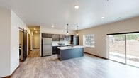 This well-appointed 2-bedroom, 2-bathroom single-story residence offers a thoughtfully designed open-concept layout with modern finishes throughout. The combined kitchen and living area serves as the heart of the home, anchored by a large center island with a white quartz countertop, undermount sink, and stylish pendant lighting. Dark espresso cabinetry contrasts beautifully with the bright countertops, while stainless steel appliances—including a refrigerator, electric range, and microwave—complete the kitchen. Light wood-look flooring runs throughout the main living areas, contributing to a clean, contemporary aesthetic. Natural light filters in through multiple windows fitted with blinds. A charming entry door with a glass panel leads into the spacious living area. Both bedrooms feature plush carpeting, ceiling fans with light fixtures, and windows that bring in natural light. The primary bedroom connects to a full bathroom equipped with a sleek vanity, white quartz countertop, matte black fixtures, and access to a walk-in closet with built-in shelving. The second bathroom includes a tub/shower combo and a matching dark-cabinetry vanity. A dedicated in-unit laundry room houses a full-size front-loading washer and dryer. A separate closet provides additional storage.