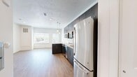 This single-floor studio is thoughtfully designed to maximize its compact footprint, combining the kitchen and living area into one cohesive, open-concept space. The kitchen is a standout feature, outfitted with dark espresso-toned cabinetry extending to the ceiling, white quartz countertops, and a full suite of stainless steel appliances including a refrigerator, dishwasher, microwave, and range. A peninsula with a white countertop provides additional workspace and serves as a natural divider between the kitchen and living area. Pendant lighting above adds a modern, polished touch. The living area benefits from large windows that invite abundant natural light and frame views of the surrounding mountain landscape. Light wood-tone luxury vinyl plank flooring runs throughout the entire space, contributing to a warm, cohesive aesthetic. The textured ceiling adds subtle visual depth. The bathroom continues the contemporary design language with matching dark cabinetry, white quartz countertops, an undermount sink, a large wall-mounted mirror, and wood-tone flooring. Clean white walls throughout the unit maintain a bright, neutral backdrop that enhances the sense of openness across the entire space.