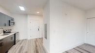 Located at 77 William St in Belleville, NJ, this efficiently designed single-floor studio unit offers a thoughtfully laid-out living space with contemporary finishes throughout. The open living area features light gray hardwood-style flooring, crisp white walls, and a window fitted with a navy roller shade, allowing natural light to brighten the room. A wall-mounted PTAC unit provides climate control.

The kitchen is a standout feature, showcasing sleek dark gray cabinetry with matte black hardware, a quartz countertop, a textured tile backsplash, and a full suite of stainless steel appliances including a refrigerator, electric range, over-the-range microwave, and dishwasher. The clean, modern aesthetic makes the kitchen both functional and visually appealing.

The bathroom is finished with large-format gray tile flooring and textured accent wall tile, lending a sophisticated feel. It includes a walk-in shower with grab bars, a toilet, and a vanity with mirror. A stacked GE washer and dryer unit is conveniently integrated into the bathroom area, adding significant in-unit utility. Recessed lighting and modern fixtures complete the polished look of this well-appointed unit.