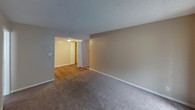 This single-story unit is laid out with a practical, functional floor plan that connects the main living area, kitchen, bedrooms, and bathrooms in a compact, efficient arrangement. The living room features neutral beige walls, wall-to-wall carpeting, and a textured ceiling, providing a clean and understated backdrop. A dedicated entry area with a wood-style floor transitions seamlessly into the carpeted living space, with an adjacent opening leading into the kitchen.

The galley-style kitchen is outfitted with dark espresso-toned cabinetry, light speckled countertops, a stainless steel sink, and white appliances including a coil-top range and a full-size refrigerator. Wood-style flooring runs throughout the kitchen, adding contrast to the darker cabinetry.

Two carpeted bedrooms offer adequate space for furnishings, each with windows that allow in natural light. The primary bedroom includes a walk-in closet with a rod and shelf system, as well as a private en-suite bathroom. This bathroom features a tub-shower combination with tile surround, a vanity with a speckled countertop, and a wall-mounted mirror. A second full bathroom mirrors this layout, also featuring a tub-shower combination with tile surround and similar finishes. Textured ceilings are consistent throughout the unit.