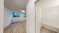 Located at 619 Woodbine Ave in Toronto's East End neighbourhood of The Beach, this one-bedroom, one-bathroom unit offers an efficiently designed single-floor layout with modern finishes throughout. Light wood laminate flooring runs continuously across the space, creating a cohesive and clean aesthetic.

The kitchen is thoughtfully appointed with white shaker-style cabinetry — including tall upper cabinets for ample storage — dark countertops, a white subway tile backsplash, and a full suite of stainless steel appliances including a refrigerator, stove, and dishwasher.

The bedroom is a well-proportioned private retreat featuring crisp white walls, a panel door, and direct access to the adjoining living area. A dedicated window with a radiator beneath it provides both natural light and reliable heating, with views of the surrounding greenery.

The bathroom is finished with floor-to-ceiling white subway tile surrounding a full soaker tub and shower combination, paired with a clean white vanity and mirror — delivering a bright, timeless look.

Throughout the unit, white walls, consistent flooring, and multiple windows contribute to an open and airy feel despite the compact footprint. Radiator heating is present in multiple rooms, ensuring year-round comfort in this well-maintained Toronto residence.
