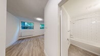 Located at 619 Woodbine Ave in Toronto's East End neighbourhood of The Beach, this one-bedroom, one-bathroom unit offers an efficiently designed single-floor layout with modern finishes throughout. Light wood laminate flooring runs continuously across the space, creating a cohesive and clean aesthetic.

The kitchen is thoughtfully appointed with white shaker-style cabinetry — including tall upper cabinets for ample storage — dark countertops, a white subway tile backsplash, and a full suite of stainless steel appliances including a refrigerator, stove, and dishwasher.

The bedroom is a well-proportioned private retreat featuring crisp white walls, a panel door, and direct access to the adjoining living area. A dedicated window with a radiator beneath it provides both natural light and reliable heating, with views of the surrounding greenery.

The bathroom is finished with floor-to-ceiling white subway tile surrounding a full soaker tub and shower combination, paired with a clean white vanity and mirror — delivering a bright, timeless look.

Throughout the unit, white walls, consistent flooring, and multiple windows contribute to an open and airy feel despite the compact footprint. Radiator heating is present in multiple rooms, ensuring year-round comfort in this well-maintained Toronto residence.