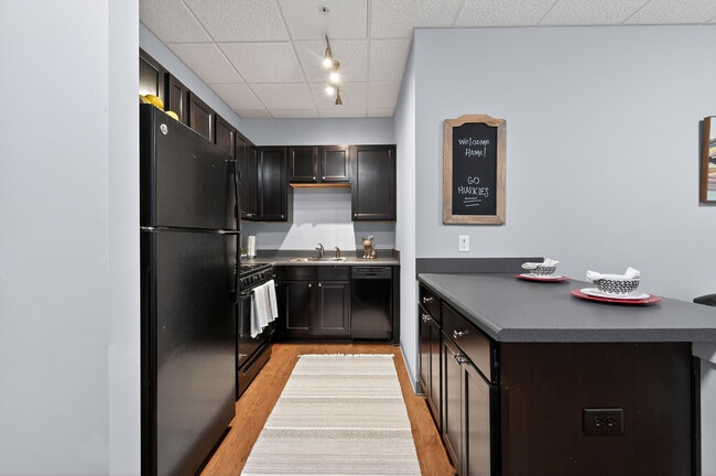 Modern Kitchen with Wood-Style Flooring and Black Appliances at University Plaza NIU Apartments - University Plaza Apartments