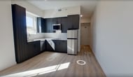 This 290 square foot studio apartment in Salt Lake City offers a thoughtfully designed living space on a single floor. The interior showcases a contemporary aesthetic with light-colored walls and sleek laminate flooring throughout, creating a sense of continuity and spaciousness.

The efficiently designed kitchen boasts dark wood cabinetry, providing a striking contrast to the light surroundings. Stainless steel appliances, including a refrigerator and built-in microwave, add a modern touch. A window above the sink allows natural light to illuminate the cooking area.

The bathroom features clean lines with a white toilet, shower area, and vanity. A chrome towel bar and recessed lighting contribute to the modern feel. The main living area is versatile, with ample wall space for furniture arrangement and a large window that floods the room with natural light, offering views of the surrounding area.

Recessed lighting fixtures are strategically placed throughout the apartment, ensuring well-lit spaces during evening hours. The layout maximizes the use of available space, with clear divisions between functional areas despite the open-plan design. This studio apartment is ideal for those seeking a minimalist, low-maintenance lifestyle in an urban setting.