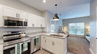 Located at 3169 Northwest Blvd in Upper Arlington, Ohio, this thoughtfully designed one-bedroom, one-bathroom residence offers a cohesive and modern living experience across its efficiently utilized single floor. The open-concept kitchen flows seamlessly into the living area, creating an inviting, connected atmosphere. The kitchen is outfitted with crisp white shaker-style cabinetry with matte black hardware, granite-look countertops, stainless steel appliances including a range, over-the-range microwave, and dishwasher, and a peninsula with an undermount sink topped by a statement pendant light. Light wood-style flooring anchors the kitchen and entry area. The living room features plush carpeting, neutral soft-gray walls, and a large window with blinds that allows natural light to fill the space. The spacious primary bedroom, also carpeted, includes a bright window and access to the dedicated closet. The bathroom is finished with a white vanity topped with granite-look counters, a bold black-framed mirror, matte black fixtures, and a tub-shower combination. Soft, neutral tones throughout the home create a calm and modern ambiance well-suited for comfortable everyday living.
