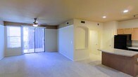 This single-floor residence in Richardson, Texas presents a thoughtfully designed open layout that maximizes the sense of space throughout the main living area. The living room is finished with wall-to-wall carpet and features a ceiling fan with a light fixture, providing both comfort and overhead illumination. Recessed lighting adds to the well-lit atmosphere of the space.

A standout architectural detail is the arched passageway that elegantly divides the living area from the adjacent hallway, lending a classic, refined character to the interior. The warm, neutral-toned walls complement the light-colored carpet, creating a cohesive and inviting atmosphere throughout.

Natural light filters into the living area through a full-length sliding glass door dressed with vertical blinds, offering access to an outdoor area while brightening the interior. To the right, a partial view reveals a countertop and cabinetry, suggesting a kitchen or dining space nearby. Multiple HVAC vents are visible throughout the ceiling, ensuring efficient climate control. The overall design is clean, functional, and move-in ready.