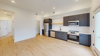 Located at 1221 N Fourth St in Philadelphia's vibrant Fishtown/North Philadelphia neighborhood, this thoughtfully designed one-bedroom, one-bathroom unit delivers a clean, modern aesthetic across a well-organized single floor. Light-toned hardwood floors run throughout the living areas and bedroom, lending warmth and continuity to the space.

The open-concept kitchen and living area serves as the heart of the unit. The kitchen is outfitted with sleek dark cabinetry, a natural wood open shelf, white quartz countertops, stainless steel appliances including a refrigerator, range, microwave, and dishwasher, and a modern matte black faucet. Large windows allow abundant natural light to fill the area, offering pleasant outdoor views of surrounding greenery.

The bedroom is a bright, comfortable retreat featuring a ceiling fan, a sliding closet, and a window that brings in additional natural light. Clean white walls and the same light hardwood flooring carry through, maintaining the unit's cohesive, contemporary feel.

The bathroom showcases a refined design with stone-look tile flooring, a warm wood vanity with a white countertop, a frameless glass walk-in shower with white subway tile, and matte black hardware accents throughout. A utility room and hallway round out the layout, providing practical storage and circulation space. The overall ambiance is bright, clean, and move-in ready.
