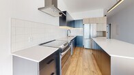 Located at 3555 Rue Saint-Antoine O in Montreal, this well-appointed one-bedroom, one-bathroom unit offers a thoughtfully designed layout across a generous single floor. Warm-toned hardwood flooring flows throughout, complementing the bright white walls and clean modern aesthetic visible in every room. The open-concept kitchen and living area serves as the heart of the space, featuring a striking two-tone kitchen with matte navy and light wood cabinetry, a large central island with a white quartz countertop, stainless steel appliances, a bold range hood, and a white subway tile backsplash — an ideal setup for both cooking and entertaining. The living area is bathed in natural light, with access to a private balcony that brings in additional brightness. The bedroom is a calm, well-proportioned retreat with a built-in closet and ample natural light. A versatile den provides flexible space for a home office or guest area. The bathroom is finished to a high standard, featuring large-format floor tiles, a floating wood-grain vanity, an integrated white sink, a round black-framed mirror, and a soaking tub. A dedicated laundry closet with stacked washer and dryer adds everyday convenience. Two additional closets and a hallway complete the practical, well-organized floor plan.