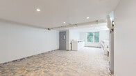 Located at 1435 51st Street in North Bergen, NJ, this shared laundry facility offers a clean, well-maintained environment designed for efficient communal use. The space is generously sized, providing ample room for multiple users at once. The flooring throughout features a durable, earth-toned stone tile in a varied mosaic pattern, lending a practical yet visually appealing finish to the room.

The laundry area is equipped with a full lineup of front-loading washing machines and matching dryers arranged along the walls, offering substantial capacity to serve building residents. Recessed ceiling lights and fluorescent tube fixtures ensure bright, even illumination throughout. A utility sink is also present, adding to the room's functionality.

Natural light filters in through a window overlooking a lush, green tree canopy, contributing a pleasant outdoor connection to an otherwise utilitarian space. The walls are finished in clean white and light gray tones, maintaining a fresh, orderly appearance. A dedicated utility area houses a large water heater and associated piping infrastructure. The space is accessed via a solid door with a window panel, and a fire safety system is visibly installed. Overall, the facility is thoughtfully designed to balance practicality with a tidy, comfortable environment.