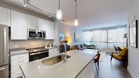 This single-floor residence showcases a contemporary open-concept design that seamlessly integrates the kitchen, dining, and living areas into one cohesive, light-filled space. The kitchen is a standout feature, equipped with stainless steel appliances including a gas range, microwave, and refrigerator. White shaker cabinetry pairs elegantly with a neutral tile backsplash, while a generous island with a quartz countertop and undermount sink serves as the centerpiece, topped by sleek pendant lighting. Track lighting along a curved rail adds additional illumination throughout the cooking space.

Wood-look flooring flows throughout the main living area, which is anchored by floor-to-ceiling windows that flood the space with natural light and offer outdoor views. The living room provides a comfortable, well-proportioned layout suited for both relaxing and entertaining.

The bedroom features plush carpeting, a glass door providing natural light and outdoor access, and dual sliding-door closets offering generous storage. A private bathroom sits conveniently adjacent. A dedicated in-unit laundry area houses a stacked washer and dryer, adding practical convenience. Throughout, the design maintains a clean, modern aesthetic with a neutral palette and thoughtful finishes.