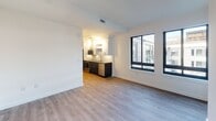 Located at 1250 Half St SE in Washington, DC's vibrant Navy Yard neighborhood, this single-floor residence showcases a clean, contemporary design with an open and airy layout. The living area features smooth light gray wood-style flooring and crisp white walls, creating a bright, neutral canvas that fills naturally with light from large, black-framed windows that frame views of the surrounding urban streetscape.

The kitchen is thoughtfully designed with two-tone cabinetry — dark navy lower cabinets paired with white uppers — and is equipped with stainless steel appliances including a range, over-the-range microwave, dishwasher, and refrigerator. Stone-look countertops and a geometric hexagonal tile backsplash add texture and visual interest, while a stainless steel undermount sink completes the polished look.

The bedroom offers a generous footprint with the same consistent hardwood-style flooring, clean white walls, and ample space for furnishings. The bathroom is finished with large-format light tile flooring, a dark-vanity with stone countertop, and a full soaking tub with shower combination, all accented by brushed nickel fixtures and recessed lighting. The overall floor plan, visible in the dollhouse view, reveals a well-proportioned layout with barn-style interior doors adding a modern design touch throughout.