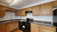 Located at 6851 Sharon Ct in Columbus, Ohio, this multi-floor property spans three levels, offering generous living space throughout. The kitchen is a standout feature, showcasing warm honey-toned oak cabinetry that extends to the ceiling, providing an abundance of storage. Dark granite-style countertops offer a rich contrast against the light-colored walls, creating a classic and functional aesthetic. Black appliances, including an electric range with a built-in overhead vent hood and a dishwasher, are thoughtfully integrated into the layout. The kitchen's L-shaped configuration maximizes workspace and flow, making it well-suited for everyday cooking and meal preparation. Wood-style flooring runs underfoot, adding warmth to the space, while track lighting illuminates the work areas effectively. The textured ceiling adds a subtle architectural detail consistent throughout. With three floors of living space, this property offers versatile room configurations to accommodate a variety of lifestyle needs. The overall aesthetic is practical and inviting, combining classic wood tones with durable finishes for a home that is both functional and comfortable.