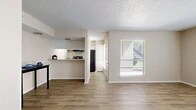 Located in Arlington, Texas, this single-story residence offers a thoughtfully designed layout encompassing one bedroom and one bathroom. The open-concept living room serves as the heart of the home, bathed in natural light from two large windows dressed with horizontal blinds. Wood-look tile flooring flows seamlessly throughout the main living and kitchen areas, creating a cohesive and easy-to-maintain foundation.

The kitchen is defined by a pass-through counter with a granite-style surface that opens to the living space, promoting an interactive and connected feel. White cabinetry lines the upper portion of the kitchen wall, complemented by a black refrigerator, range, and an overhead ventilation hood. A textured popcorn ceiling adds character throughout the home.

The spacious primary bedroom features plush wall-to-wall carpeting, a mirrored sliding closet, and a dedicated window that allows natural light to filter in. Neutral warm-toned walls carry throughout the entire residence, lending a calm and cohesive aesthetic. A hallway connects the bedroom to the full bathroom, which showcases a granite-topped vanity with white cabinetry. The bathroom also provides access to a walk-in closet area, adding practical storage to the overall floor plan.