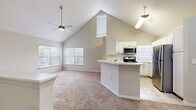 This single-floor, 1-bedroom, 1-bathroom residence offers a thoughtfully designed layout that maximizes both comfort and functionality. The living area immediately impresses with dramatic vaulted ceilings that soar overhead, creating an expansive, airy atmosphere. A ceiling fan with a light fixture serves the space, while multiple windows—including a distinctive oval accent window—flood the room with natural light and offer views of the surrounding neighborhood. Soft, neutral-toned carpet runs throughout the living and bedroom areas, contributing to a warm ambiance.

The kitchen is open to the living space and features white cabinetry, a classic subway tile backsplash, and light tile flooring. A peninsula-style breakfast bar provides casual seating and additional counter space. Stainless steel appliances—including a refrigerator, range, and over-the-range microwave—offer a modern, functional finish. The vaulted ceiling extends into the kitchen, further enhancing the sense of openness.

The primary bedroom is a well-proportioned retreat with carpeted floors, a ceiling fan, and a large window that brings in ample daylight. The full bathroom is clean and straightforward, featuring tile flooring, a tub-shower combo with tiled surround, a single vanity with storage, and a large mirror. A hallway connects the main living areas to the private quarters, completing this efficient and inviting floor plan.