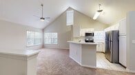 This single-floor, 1-bedroom, 1-bathroom residence offers a thoughtfully designed layout that maximizes both comfort and functionality. The living area immediately impresses with dramatic vaulted ceilings that soar overhead, creating an expansive, airy atmosphere. A ceiling fan with a light fixture serves the space, while multiple windows—including a distinctive oval accent window—flood the room with natural light and offer views of the surrounding neighborhood. Soft, neutral-toned carpet runs throughout the living and bedroom areas, contributing to a warm ambiance.

The kitchen is open to the living space and features white cabinetry, a classic subway tile backsplash, and light tile flooring. A peninsula-style breakfast bar provides casual seating and additional counter space. Stainless steel appliances—including a refrigerator, range, and over-the-range microwave—offer a modern, functional finish. The vaulted ceiling extends into the kitchen, further enhancing the sense of openness.

The primary bedroom is a well-proportioned retreat with carpeted floors, a ceiling fan, and a large window that brings in ample daylight. The full bathroom is clean and straightforward, featuring tile flooring, a tub-shower combo with tiled surround, a single vanity with storage, and a large mirror. A hallway connects the main living areas to the private quarters, completing this efficient and inviting floor plan.