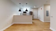 Located at 333 State St in Bridgeport, Connecticut, this single-floor residential unit offers a thoughtfully designed layout with modern finishes and a clean, contemporary aesthetic. The open-concept kitchen is a standout feature, equipped with stainless steel appliances — including a refrigerator, range, and microwave — complemented by white upper cabinetry, dark wood lower cabinets, and a herringbone-pattern tile backsplash. A peninsula with a white quartz countertop and an undermount sink doubles as a breakfast bar, illuminated by a pair of striking black pendant lights. Light-toned hardwood flooring flows seamlessly throughout the living and bedroom areas, creating a warm and cohesive atmosphere. The living area is open and airy, benefiting from natural light streaming through a tall window with views of the surrounding streetscape. The bedroom is generously proportioned, featuring the same hardwood flooring and a large window that fills the room with daylight. The full bathroom is finished with large-format white floor tiles, full-height wall tiling in the shower/tub combination, a dark wood vanity with a white countertop, and a backlit mirror, bringing a polished, spa-like quality to the space. Overall, the unit presents a well-appointed, move-in-ready interior with a consistent modern design language.