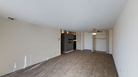 This single-floor residence offers an open and functional layout with a clean, modern aesthetic. The main living area is spacious and filled with natural light, showcasing warm wood-style hardwood flooring that extends throughout the space, providing a cohesive and inviting feel underfoot. Neutral-toned walls complement the overall brightness of the interior, creating a versatile backdrop for a variety of furnishing styles.

A ceiling fan with a light fixture is centrally positioned to ensure comfortable airflow across the living area. Built-in shelving and a large closet with open hanging rods provide ample storage and organizational options directly within the main living space—a practical and convenient design feature.

The kitchen is open to the living area and is outfitted with dark, charcoal-toned cabinetry that offers a contemporary contrast to the lighter walls and flooring. The kitchen's semi-open configuration allows for easy interaction between the cooking and living zones, making the space well-suited for both everyday living and entertaining.

Overhead lighting in the kitchen provides functional illumination, while the overall layout prioritizes efficiency and flow. The single-floor design ensures seamless accessibility throughout, making this a practical and well-appointed space.