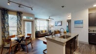This single-floor residence offers a thoughtfully designed open-concept layout that seamlessly connects the kitchen, dining, and living areas. The kitchen is a standout feature, equipped with dark espresso cabinetry, stainless steel appliances, recessed lighting, and a generously sized granite-topped island with bar seating — ideal for casual dining or entertaining. Wood-style flooring flows throughout the main living areas, adding warmth and continuity to the space.

The living room is bright and welcoming, benefiting from large windows dressed with patterned drapes that invite abundant natural light. A ceiling fan overhead and a wall-mounted television make the space both comfortable and functional.

The bathroom features an L-shaped double-vanity layout with matching granite countertops, dark cabinetry with brushed nickel hardware, and a framed mirror — providing ample storage and counter space.

The bedroom is a calm and comfortable retreat, featuring a ceiling fan, a large window with exterior views, and plush carpeting underfoot. A dedicated entry area with a keypad-secured door adds a layer of convenience and security. Overall, the residence combines modern finishes with a practical, cohesive design that suits a contemporary lifestyle.