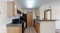 Located at 6755 Brandon Village Way in Canal Winchester, Ohio, this single-floor unit offers a practical and functional layout designed for comfortable everyday living. The galley-style kitchen is well-appointed with light oak cabinetry providing ample storage, dark granite-look countertops, and a full suite of black appliances including an electric range, refrigerator, and built-in range hood. A double basin sink and a peninsula counter with a breakfast bar add to the kitchen's utility. Wood-look plank flooring runs throughout the kitchen and main living areas, offering durability and a clean aesthetic. The open area adjacent to the kitchen provides flexible living and dining space, filled with natural light and connected to the rest of the unit through wood-trimmed doorways. The bedrooms feature neutral-toned carpet, white walls, and windows with blinds that allow for natural light and outdoor views of the surrounding greenery. The full bathroom is equipped with a single-sink vanity with a wood-framed mirror, a toilet, and a tub-shower combo with a curtain rod. Textured ceilings are present throughout, and the consistent warm wood trim detailing on doors and baseboards ties the interior together with a cohesive, traditional feel.
