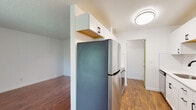 This single-floor unit offers a thoughtfully updated layout that balances functionality and comfort throughout. The galley-style kitchen is a standout feature, showcasing white shaker cabinetry with matte black hardware, light countertops, a white subway tile backsplash, a stainless steel undermount sink with a black matte faucet, and stainless steel appliances including a refrigerator and range. Warm wood-look flooring runs through the kitchen and connects seamlessly to the adjoining living areas. The living room is generously proportioned, with rich hardwood-style flooring, a textured ceiling, and large sliding glass doors flanked by a window that invite abundant natural light and open to a view of lush greenery outside. Vertical blinds provide privacy and light control. The bedroom is a comfortable retreat finished with plush carpeting, a wide mirrored sliding closet, and a window overlooking the surrounding neighborhood. The full bathroom is cleanly finished in white, featuring a single-sink vanity with black hardware, a framed mirror, a soaking tub with shower, and warm wood flooring. The overall ambiance is fresh and move-in ready, with consistent modern finishes throughout.