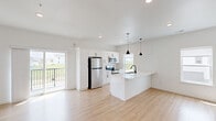Located at 402 Fast Ln in Hudson, Iowa, this three-bedroom, three-bathroom home spans three floors, offering a well-organized layout with distinct living zones across each level. The entry level provides a welcoming foyer with light wood-style flooring and dark-carpeted staircase with black metal railing, setting a clean, modern tone throughout.

The main living floor serves as the heart of the home, featuring an open-concept kitchen and living area filled with natural light from multiple windows and sliding glass door access to a private balcony. The kitchen is appointed with crisp white shaker cabinetry, stainless steel appliances, a built-in microwave, and a large center island topped with white quartz countertops. Matte black pendant lights and hardware add a contemporary contrast against the bright, neutral palette.

The upper floor houses the bedrooms, each finished with the same warm wood-style flooring and clean white walls. The bedrooms feature double-door closets and panel-style doors with black hardware. The three bathrooms are well-appointed, including a tub-shower combination and a separate walk-in glass-door shower with a white vanity and modern light fixtures. Throughout the home, the consistent use of light tones, recessed lighting, and thoughtful design details create a cohesive, move-in-ready living environment.