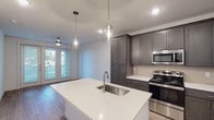 This well-appointed one-bedroom, one-bathroom residence in Spring, Texas offers a thoughtfully designed single-level layout with modern finishes throughout. The open-concept kitchen serves as the heart of the home, showcasing dark gray shaker-style cabinetry that extends to the ceiling for generous storage, crisp white quartz countertops, and a full suite of stainless steel appliances including a refrigerator, range, and built-in microwave. A central kitchen island with an undermount sink and elegant pendant lighting adds both functionality and style, while a light gray subway tile backsplash completes the contemporary aesthetic. Light wood-style flooring flows through the main living areas, creating a warm and cohesive feel. The bedroom offers a comfortable, carpeted retreat with a ceiling fan and a window fitted with blinds that allows natural light and greenery views. The bathroom is finished with a granite-topped vanity, a large frameless mirror, and a glass-enclosed walk-in shower with white tile surround. A dedicated in-unit stacked washer and dryer adds everyday convenience. Recessed lighting and clean white walls throughout contribute to a bright, modern ambiance ideal for contemporary living.