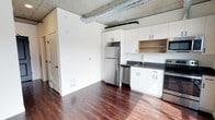 Located at 624 Yale Ave N in Seattle's vibrant South Lake Union neighborhood, this single-floor unit showcases a contemporary industrial aesthetic that blends modern finishes with raw architectural character. The exposed concrete ceiling and visible ductwork lend an urban loft-like atmosphere, while rich, dark hardwood flooring grounds the space with warmth and elegance throughout.

The kitchen is thoughtfully designed with white shaker-style cabinetry offering ample storage, complemented by dark countertops that provide a striking contrast. Stainless steel appliances — including a full-size refrigerator, dishwasher, and range — complete the functional and stylish cooking area. Open shelving adds a casual, accessible touch to the upper cabinetry arrangement.

The open-concept layout maximizes the sense of space, allowing the kitchen and living areas to flow seamlessly together. Clean white walls provide a bright, neutral backdrop that enhances the natural light throughout. The overall ambiance strikes a balance between industrial edge and modern comfort, making it an ideal setting for urban living in one of Seattle's most dynamic and walkable neighborhoods.