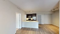 This single-floor residence showcases a contemporary design with a cohesive neutral palette and quality finishes throughout. The open-concept layout connects the living area to a well-appointed kitchen, which features dark espresso cabinetry, a white subway tile backsplash, stainless steel appliances including a range, microwave, and refrigerator, and a peninsula with a white countertop and integrated sink. Light wood-tone luxury vinyl plank flooring runs through the main living areas, complementing the bright, airy atmosphere enhanced by a ceiling fan and track lighting.

The living space is generously proportioned, with a sliding glass door providing access to an outdoor area and allowing natural light to fill the room. Bedrooms are finished with plush neutral carpet and include closets with built-in shelving. One bedroom offers direct access to a dedicated laundry area housing a full-size washer and dryer.

Two bathrooms serve the unit, each featuring dark wood vanities with white countertops and light wood-tone flooring. One bathroom includes a soaking tub with tiled surround, while the other offers a tub-shower combination. The overall ambiance is clean, modern, and move-in ready.