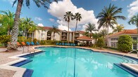 This single-story residence is part of a well-appointed tropical community defined by its Mediterranean-inspired architectural style. The buildings feature warm stucco exteriors, red clay tile rooflines, and private balconies that overlook the lushly landscaped grounds. Towering palm trees frame the property, creating a resort-like atmosphere that is characteristic of South Florida living.

The standout feature of the community is the expansive outdoor swimming pool, which serves as a central gathering point. The generously sized pool is surrounded by a spacious deck furnished with bright blue lounge chairs, providing ample room for sunbathing and relaxation. A covered cabana pavilion anchors the pool area, offering a shaded retreat with additional seating and amenities for residents. The surrounding landscaping is verdant and well-maintained, with dense tropical greenery, mature palms, and manicured shrubs that enhance the sense of privacy and seclusion.

The open-air setting benefits from abundant natural light throughout the day, and the overall ambiance evokes a laid-back, vacation-inspired lifestyle. The combination of classic architectural detailing and resort-style outdoor amenities makes this a distinctive and inviting community environment.
