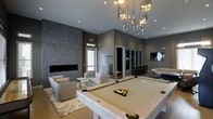 This single-floor space is a sophisticated game and lounge area that combines modern design with functional recreational amenities. At its centerpiece sits a light-toned pool table, positioned beneath a striking sculptural chandelier composed of mixed metallic and glass pendants that serve as a dramatic focal point overhead. The room is finished with smooth gray walls, recessed lighting, and elevated ceilings that lend a sense of openness and volume to the space.

A textured stone accent wall adds depth and visual contrast along one side of the room, flanking a sleek, linear gas fireplace set low to the ground. In front of the fireplace, a comfortable seating arrangement features neutral-toned lounge chairs atop a plush area rug, creating an inviting conversation area. On the opposite end, additional casual seating and a bar-style counter area provide further space for socializing and entertainment. A cue rack and gaming storage are neatly integrated into the design. Natural light filters in through a window near the fireplace, complementing the warm, ambient glow of the interior lighting throughout the space.
