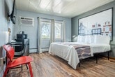Located at 3177 E Washington Ave in Madison, Wisconsin, this efficiently designed single-floor unit offers a practical and comfortable living arrangement. The layout includes a generously sized bedroom, a full bathroom, and a connecting hallway.

The bedroom serves as the centerpiece of the space, featuring warm wood-look flooring, soft gray walls, and a clean white panel ceiling with flush-mount lighting. Natural light filters in through multiple windows dressed with light curtains, offering views of surrounding trees. The room is well-appointed with a queen bed, a wall-mounted flat-screen television, a compact desk and seating area, a mini refrigerator, and a microwave — providing essential conveniences. A wall-mounted air conditioning unit ensures year-round comfort, complemented by baseboard heating.

The bathroom is bright and clean, finished with classic mosaic tile flooring in warm earth tones and crisp white walls. It includes a full tub-shower combo with a curtain, a toilet, and a streamlined vanity with counter space.

A short hallway connects the entry to the bedroom, providing a defined transition into the living area. Overall, the space strikes a balance between functionality and comfort, making it a practical choice for visitors to the Madison area.