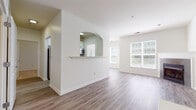 Located at 54 Republic Dr in Bloomfield, CT, this single-floor residence offers a thoughtfully designed layout with a bright, open feel throughout. The main living area is generously proportioned, featuring vaulted ceilings, light-toned hardwood-style flooring, and a tile-surround fireplace that serves as a central focal point. Large windows allow ample natural light to fill the space while offering views of the surrounding greenery.

The kitchen is connected to the living area via a distinctive arched pass-through with a built-in ledge, maintaining an open visual connection between spaces. The kitchen is equipped with white cabinetry accented by matte black hardware, light countertops, stainless steel appliances, and a gas range, providing a clean, functional workspace.

The bedroom features neutral carpet, a window overlooking the outdoors, and easy access to adjacent spaces. A dedicated laundry area accommodates a full-size washer and dryer. The bathroom includes hardwood-style flooring and accessibility-friendly grab bar supports.

An attached garage with an automatic opener and concrete flooring completes the residence, offering convenient and secure parking or additional storage capacity.