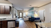 Located in Destin, Florida, this thoughtfully designed guest suite delivers a cohesive coastal aesthetic throughout its two bedrooms and two bathrooms. The open-concept living area immediately draws attention with its bold teal and white horizontal striped accent wall, wood-look flooring, and ceiling fan — setting a relaxed, beach-inspired tone. The living room flows seamlessly into the dining area, which features a complementary geometric-patterned accent wall in aqua tones. The kitchen is well-appointed with rich dark wood cabinetry, granite countertops, a full suite of stainless steel appliances, and a tile backsplash, offering ample storage and counter space. The primary bedroom continues the nautical theme with a striped accent wall in navy and teal, plush carpeting, a ceiling fan, and a dedicated closet. The second bedroom is comfortably sized with carpeted floors and ceiling fan. Both bathrooms echo the coastal color palette, with one featuring a glass-enclosed walk-in shower, dark wood vanity, granite counters, and wood-look flooring. Accessibility features including grab bars are present in the bathrooms. Additional highlights include multiple closets throughout, a dedicated laundry space, and a private patio for outdoor enjoyment.