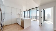 Located in San Diego's vibrant downtown corridor, this high-rise residence offers a sleek, contemporary design defined by floor-to-ceiling black-framed windows that flood the interior with natural light and frame expansive views of the city skyline and surrounding mountains. Light-toned hardwood flooring runs throughout the open-concept living areas, complementing the clean white walls and contributing to a bright, airy atmosphere.

The kitchen is a standout feature, showcasing white shaker cabinetry extending to the ceiling, a marble-veined quartz waterfall island with an undermount sink and industrial-style faucet, and a full suite of stainless steel appliances including a gas range, built-in microwave, refrigerator, and dishwasher. Pendant lighting above the island adds a refined finishing touch. The living area flows seamlessly from the kitchen, with direct access to a private balcony overlooking the downtown San Diego skyline.

The bathrooms are finished with large-format neutral tile and include built-in shelving for storage. One bathroom features a glass-enclosed walk-in shower with a rain showerhead and bench, while a second offers a soaking tub with tiled surround. Throughout, the design prioritizes clean lines, quality finishes, and a cohesive modern aesthetic.