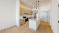 Located at 2220 Berryhill Road in Charlotte, NC, this one-bedroom, one-bathroom unit offers a thoughtfully designed single-floor layout with contemporary finishes throughout. The open-concept living area seamlessly connects the kitchen, dining, and living spaces, creating an airy and functional environment. The kitchen is a standout feature, outfitted with light wood cabinetry, stainless steel appliances including a range, over-the-range microwave, and refrigerator, complemented by a center island with a sink and pendant lighting overhead. Light-toned wood-style flooring runs throughout the main living areas, adding warmth and cohesion to the space. The bedroom is generously sized, featuring soft carpeting, a ceiling fan, and a window with natural light and exterior views. A dedicated walk-in closet with built-in wire shelving provides ample organized storage. The bathroom offers a clean, modern aesthetic with light wood vanity cabinetry, white countertops, matte black hardware accents, and a full tub-shower combination with tile surround and hardwood-style flooring. Additional conveniences include a dedicated laundry area and a utility room. The unit's neutral color palette and modern design elements create a bright, welcoming atmosphere throughout.