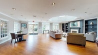 Located at 1455 Washington Blvd in Stamford, Connecticut, this single-floor amenity center is designed to offer residents a comprehensive and refined communal experience. The centerpiece of the space is a generously proportioned lounge area highlighted by a striking octagonal skylight, warm hardwood floors, a classic fireplace flanked by built-in bookshelves, and large French doors that flood the interior with natural light and provide views of the surrounding greenery. Comfortable seating arrangements and an elegant area rug create an inviting atmosphere for relaxation and social gatherings. A dedicated dining area with round tables and French glass partitions connects seamlessly to the kitchenette, which features dark cabinetry, a bar-height counter with seating, pendant lighting, and white upper cabinets. The business center is equipped with built-in workstations, computers, and a printer, set against a bold accent wall with a tray ceiling. A private conference room offers a large meeting table, wall-mounted display, and ample natural light. The well-appointed fitness center spans two connected areas, housing treadmills, ellipticals, stationary bikes, and a multi-function cable machine, all set on durable flooring with mirrored walls. Crown molding and consistent neutral tones unify the space throughout.
