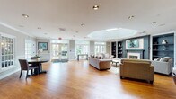 Located at 1455 Washington Blvd in Stamford, Connecticut, this single-floor amenity center is designed to offer residents a comprehensive and refined communal experience. The centerpiece of the space is a generously proportioned lounge area highlighted by a striking octagonal skylight, warm hardwood floors, a classic fireplace flanked by built-in bookshelves, and large French doors that flood the interior with natural light and provide views of the surrounding greenery. Comfortable seating arrangements and an elegant area rug create an inviting atmosphere for relaxation and social gatherings. A dedicated dining area with round tables and French glass partitions connects seamlessly to the kitchenette, which features dark cabinetry, a bar-height counter with seating, pendant lighting, and white upper cabinets. The business center is equipped with built-in workstations, computers, and a printer, set against a bold accent wall with a tray ceiling. A private conference room offers a large meeting table, wall-mounted display, and ample natural light. The well-appointed fitness center spans two connected areas, housing treadmills, ellipticals, stationary bikes, and a multi-function cable machine, all set on durable flooring with mirrored walls. Crown molding and consistent neutral tones unify the space throughout.