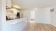 Located at 150 W Hill Ave in Fullerton, California, this one-bedroom, one-bathroom residence spans two floors, offering a practical and well-organized layout. The main floor encompasses the majority of the living space, housing the entrance, combined kitchen and living area, and bathroom, while the upper level provides a compact secondary area.

Light wood-style flooring runs throughout, creating a clean and cohesive aesthetic across the unit. The open-plan kitchen and living area serves as the heart of the home. The kitchen is outfitted with white cabinetry, a stainless steel refrigerator, gas range, dishwasher, and an undermount sink. A white peninsula counter extends into the space, providing additional prep area and a natural divider between the kitchen and living zone.

The bedroom features a textured ceiling, a broad window dressed with horizontal blinds that invites generous natural light, and a wall-mounted air conditioning unit. A sliding glass door opens to a private balcony with outdoor views of the surrounding neighborhood.

The bathroom includes a white vanity with a framed mirror, and a combined shower and bathtub enclosure. Throughout the unit, neutral white walls and light flooring contribute to a bright, clean ambiance well-suited to comfortable everyday living.