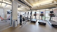 Located at 1924 8th St NW in Washington, DC's vibrant Shaw neighborhood, this fitness center offers a thoughtfully designed exercise space across a single floor. The room features an industrial-modern aesthetic, with exposed concrete ceilings, visible ductwork, and structural columns that lend the space a contemporary, urban character. Durable rubber flooring spans throughout, providing a practical and resilient surface suited for high-traffic use.

The cardio zone is well-appointed with a row of treadmills, elliptical machines, and stationary bikes, many equipped with individual digital displays. Floor-to-ceiling windows line one side of the space, flooding the room with natural light and offering open views of the surrounding Washington, DC cityscape — creating an energizing atmosphere for workouts.

The strength training area is equally comprehensive, featuring a broad selection of free weights, adjustable benches, and a variety of cable and resistance machines. A large wall-mounted flat-screen television adds a multimedia element to the space. Resistance bands are also available, anchored directly to the wall for convenient use.

The layout is organized and spacious, allowing users to move freely between equipment zones. The combination of natural light, city views, and a full suite of modern fitness equipment makes this a functional and well-rounded facility.