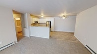Located at 1615 Webster Way in Waupaca, Wisconsin, this single-floor unit offers a well-designed, open-concept layout that seamlessly connects the kitchen and living areas. The kitchen is equipped with stainless steel appliances, including a refrigerator, range, and over-the-range microwave, complemented by crisp white cabinetry and granite-style countertops. A peninsula with a matching countertop provides additional workspace and serves as a natural divider between the kitchen and the carpeted living area, which features a ceiling fan and baseboard heating. A hallway leads to the bedrooms, each finished with plush carpet, baseboard heating, and closets with wire shelving. Natural light enters through the bedroom windows, adding brightness to the neutral color palette throughout. The bathrooms are appointed with granite-style vanity tops, white cabinetry, wood-look tile flooring, and walk-in showers with grab bars. A dedicated laundry room with wire shelving, wood-look flooring, and an in-unit washer and dryer adds everyday convenience. The consistent use of light tones, wood-look flooring in key areas, and clean finishes gives the entire space a fresh, functional character suited for comfortable living.