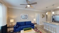 Located at 6701 Fox Rd in Raleigh, North Carolina, this single-floor home offers a well-designed layout with a warm and inviting atmosphere. The living area serves as the heart of the space, featuring smooth, neutral-toned walls, crown molding, and durable wood-style flooring that adds a clean, contemporary feel. A ceiling fan with a built-in light fixture centers the room, providing both comfort and functionality. The open layout allows for a natural flow between the living and kitchen areas, with the kitchen visible just off the main room and highlighted by a countertop bar area — ideal for casual dining or entertaining. Large doorways connect the rooms seamlessly, contributing to an airy, open feel throughout the home. The overall design balances practicality with style, offering a move-in-ready environment that suits a variety of living arrangements. Neutral wall tones and natural light work together to create a bright and comfortable interior that feels welcoming from every angle. This single-story property in Raleigh combines functional design with accessible, everyday livability.