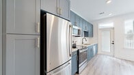 Located at 421 W Tremont Ave in Charlotte's vibrant Dilworth neighborhood, this efficiently designed single-floor unit offers a thoughtfully appointed layout comprising a kitchen, living room, and full bathroom. Light wood-tone luxury vinyl plank flooring runs throughout, creating a warm, cohesive aesthetic across the space.

The kitchen is a standout feature, showcasing slate-blue shaker-style cabinetry accented with gold hardware, a crisp white subway tile backsplash, and light quartz countertops. A full suite of stainless steel appliances — including a refrigerator, electric range, over-the-range microwave, and dishwasher — provides complete functionality within a compact, galley-style footprint.

The living area is bright and open, with multiple windows fitted with white horizontal blinds that allow natural light to filter in while offering views of the surrounding Charlotte streetscape. The clean white walls and simple trim details lend the space a fresh, modern feel.

A hallway connects the main living areas to the bathroom, which features a soaking tub and shower combo fully tiled in classic white subway tile, a white vanity with chrome hardware, and wood-look flooring that complements the rest of the unit. Recessed lighting and panel-style doors with matte black hardware complete the polished interior aesthetic.