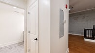 This single-floor unit offers a thoughtfully utilized layout that blends industrial character with modern finishes. The open kitchen area is equipped with stainless steel appliances, including a full-size refrigerator, range, microwave, and dishwasher. Gray shaker-style cabinetry with butcher block countertops and a subway tile backsplash add a clean, contemporary aesthetic, all set atop warm hardwood floors that extend throughout the main living area.

A defining architectural feature is the exposed white-painted brick accent wall, which lends texture and an urban loft feel to the space. Overhead, exposed ductwork and a ceiling fan contribute to the industrial design language. A black metal stair railing serves as a structural focal point, adding a bold visual contrast against the lighter walls and flooring.

The two hallways facilitate functional circulation through the unit, with one housing an electrical panel and fire safety equipment. White panel doors with dark hardware provide clean transitions between spaces.

The bathroom features a gray shaker-style vanity with a butcher block top, an undermount stainless steel sink, matte black fixtures, and a large mirror with globe lighting, all atop wood-look tile flooring—delivering a polished, cohesive finish consistent with the rest of the unit.