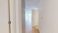 Located at 5670 Cambie St in Vancouver, BC, this efficiently designed one-bedroom, one-bathroom unit offers a clean, contemporary aesthetic throughout. Light-toned hardwood flooring runs continuously across the open layout, complementing the crisp white walls and recessed lighting that keep the space feeling bright and airy.

The kitchen is thoughtfully appointed with flat-panel cabinetry in a soft grey-white finish, a glass tile backsplash, stainless steel appliances including a full-size refrigerator and electric range, and a sleek countertop with an undermount sink. A stacked washer and dryer unit is conveniently integrated into the hallway area, adding practical in-unit laundry without sacrificing flow.

The bedroom is a calm, minimalist retreat featuring large floor-to-ceiling sliding glass doors that open to a balcony, filling the room with natural light and offering open views of the surrounding Vancouver cityscape and greenery. The hallways connect each room efficiently, maintaining a logical and uncluttered layout.

The bathroom is finished with neutral stone-toned floor tiles, a vessel sink set on a modern vanity with drawer storage, a framed mirror, and a full-size soaker tub with a tiled surround. The overall design of the unit reflects a modern, urban sensibility with quality finishes throughout.