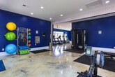 Located at 900 Meadow Glen Pkwy in Fairburn, Georgia, this single-floor fitness center is thoughtfully designed to support a well-rounded workout experience. The space is immediately distinguished by its bold royal blue walls, crisp white trim, and striking polished concrete floors that feature a marble-like swirled finish, lending the facility a clean and modern aesthetic throughout.

The layout is divided into distinct functional zones. The cardio area is generously equipped with multiple treadmills, elliptical trainers, a stationary bike, and a rowing machine, all arranged to maximize space and ease of use. Large white-framed windows line the walls, inviting an abundance of natural light and offering views of the surrounding outdoor greenery, creating an open and energizing atmosphere. A ceiling fan adds to the comfort of the space.

The strength training zone features a multi-functional cable machine, a full dumbbell rack with an accompanying weight bench, and floor-to-ceiling mirrors that enhance the sense of depth and allow users to monitor their form. Rubber floor mats are positioned under all equipment areas for safety and durability.

A decorative geometric wallpaper accent adds a refined touch near the entrance, while recessed lighting throughout ensures consistent illumination across all zones. Double glass entry doors with exterior views complete this well-appointed, community fitness facility.