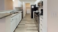 This single-floor residence offers a thoughtfully designed layout with a clean, neutral aesthetic throughout. The living area is a welcoming focal point, anchored by a fireplace and ceiling fan, with wood-look plank flooring that extends through the main living spaces. Natural light filters in through a sliding glass door, adding brightness and an airy feel to the room.

The kitchen is well-equipped with white cabinetry, granite-look countertops, and a full suite of stainless steel appliances, including an electric range, refrigerator, microwave, and dishwasher. A convenient in-unit laundry area is accessible directly from the kitchen, adding a practical and desirable amenity. The kitchen connects seamlessly to the main living and dining areas.

The bedrooms are carpeted for comfort and each feature ceiling fans with light fixtures. Closet storage is provided, with built-in shelving and hanging rods visible in at least one bedroom. The bathrooms are finished with wood-look tile flooring, white vanities with under-sink storage, and full tub-shower combinations. A welcoming entry hallway with a paneled front door completes the layout, offering a smooth transition into the main living spaces.