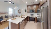 Located at 1801 Main St in Columbia, South Carolina, this single-floor residence offers a thoughtfully designed layout that balances functionality and contemporary style throughout. The open-concept kitchen serves as a central highlight, featuring rich dark-stained cabinetry, quartz countertops, a spacious peninsula with bar seating, and stainless steel appliances including a range, microwave, and dishwasher. Globe pendant lights with gold hardware add a refined finishing touch above the peninsula, while recessed lighting keeps the space bright and inviting.

The living area extends naturally from the kitchen, offering a comfortable, light-filled space with a ceiling fan and windows that allow natural light to filter in. A dedicated flex room provides additional versatility, suitable as a home office or sitting area, with neutral carpet and generous wall space.

The bedrooms are well-proportioned, each featuring plush carpet, large windows with blinds, and clean white walls that create a calm, restful atmosphere. The bathrooms are finished with large-format dark tile flooring, marble-style tiled tub surrounds, gray cabinetry with black hardware, and white quartz vanity tops—lending a polished, modern aesthetic.

A hallway near the entry accommodates a stacked washer and dryer unit, adding everyday convenience. Throughout the unit, white walls, neutral flooring, and consistent modern hardware create a cohesive and welcoming living environment.