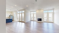 Located in Leawood, Kansas, this thoughtfully designed single-floor residence offers four bedrooms and four bathrooms within a generous, well-appointed layout. The open-concept living room is a standout centerpiece, featuring a sleek built-in fireplace, light hardwood-style flooring, recessed lighting, and a wall of French doors flanked by transom windows that flood the space with natural light and provide access to an outdoor balcony. The modern kitchen is outfitted with two-tone cabinetry — slate-blue lower cabinets paired with crisp white uppers — complemented by a tile backsplash, white quartz countertops, stainless steel appliances, and a kitchen island. Each of the four bedrooms is carpeted and features large windows with outdoor views, including treetop and balcony vistas. The primary bedroom connects directly to a private en-suite bathroom. The bathrooms throughout are consistently finished with floating gray vanities, white quartz countertops, large mirrors, and wood-look tile flooring, with at least one featuring a walk-in shower. Closet spaces include walk-in configurations with wire shelving. A dedicated laundry area houses a stacked washer and dryer unit. The overall aesthetic is clean, contemporary, and move-in ready.